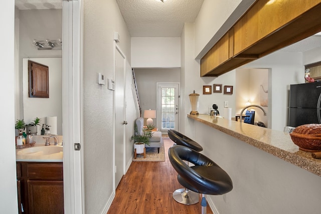 interior space featuring light stone countertops, sink, a textured ceiling, dark hardwood / wood-style flooring, and black fridge