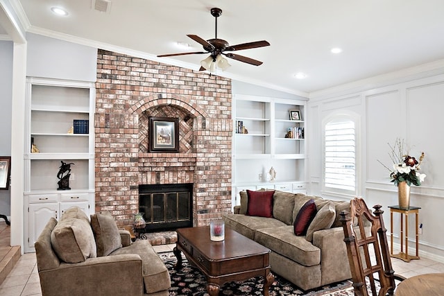 tiled living room with vaulted ceiling, a brick fireplace, ceiling fan, built in shelves, and ornamental molding