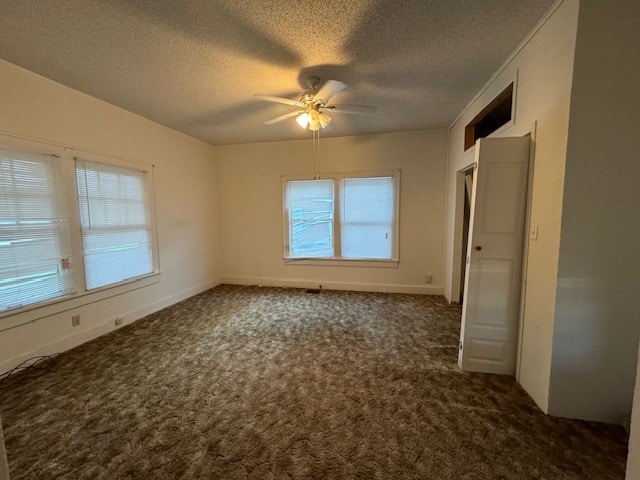 unfurnished bedroom with multiple windows, a textured ceiling, dark colored carpet, and ceiling fan