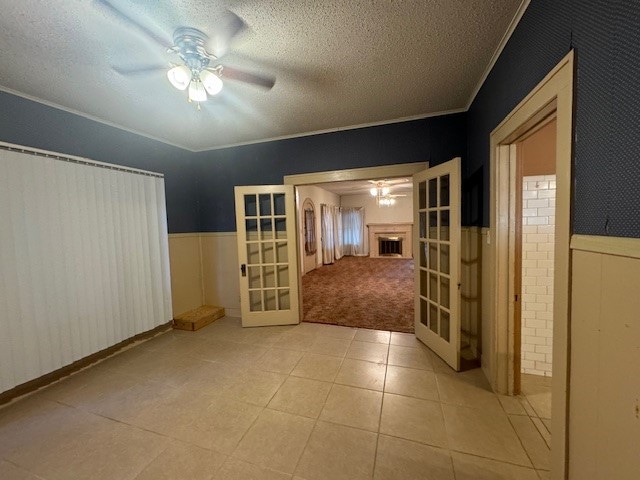 spare room featuring light tile patterned floors, a textured ceiling, crown molding, ceiling fan, and french doors