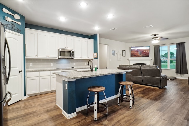 kitchen featuring wood-type flooring, white cabinets, stainless steel appliances, a center island with sink, and ceiling fan