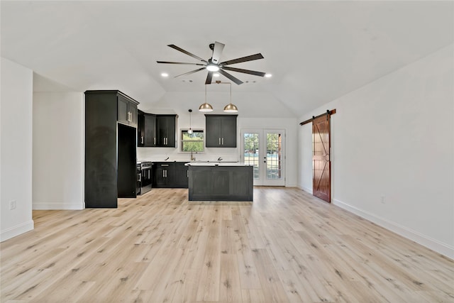 kitchen featuring light hardwood / wood-style floors, vaulted ceiling, a barn door, stainless steel range oven, and ceiling fan