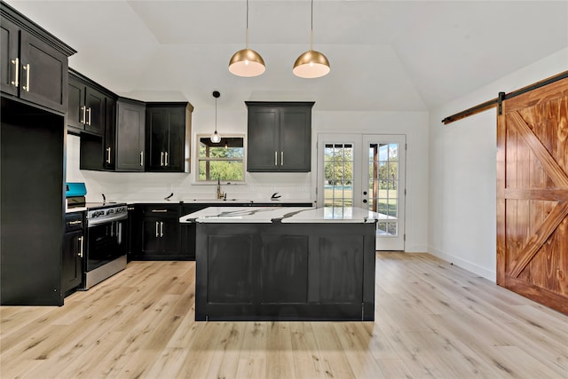 kitchen with black fridge, stainless steel stove, a kitchen island, a barn door, and decorative light fixtures