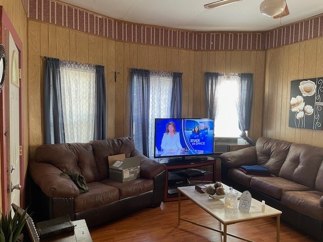 living room featuring ceiling fan, hardwood / wood-style flooring, and wooden walls