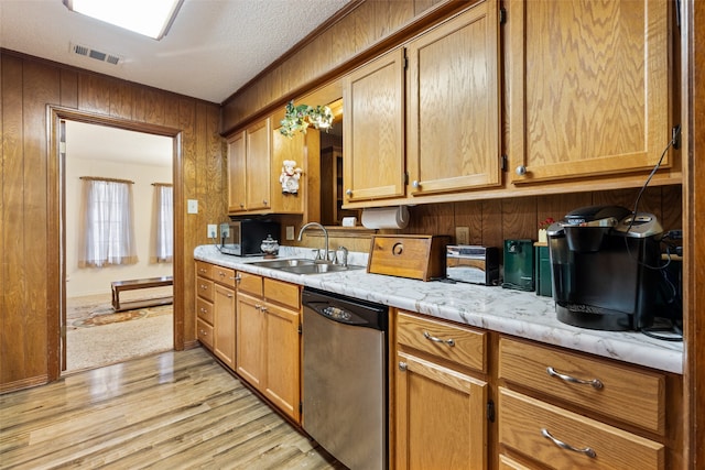 kitchen with sink, stainless steel dishwasher, a textured ceiling, wooden walls, and light hardwood / wood-style floors