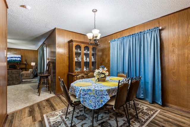 dining area featuring a notable chandelier, a textured ceiling, wood walls, and hardwood / wood-style floors