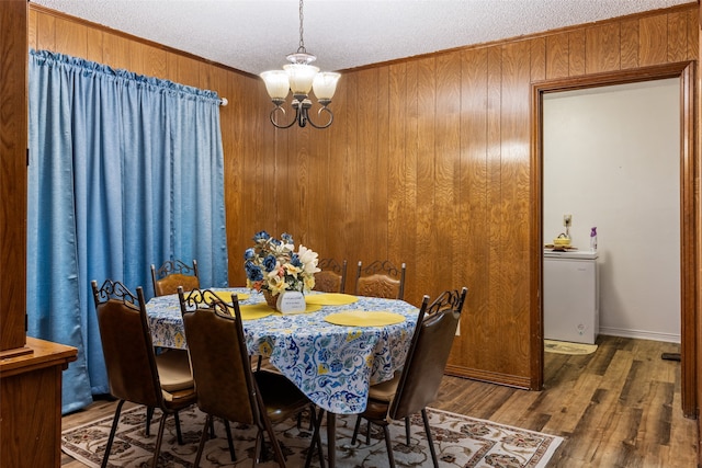 dining space with wood walls, dark hardwood / wood-style flooring, a textured ceiling, crown molding, and an inviting chandelier