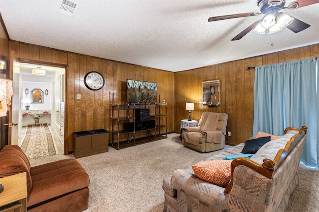 living room featuring ceiling fan, light colored carpet, a textured ceiling, and wood walls