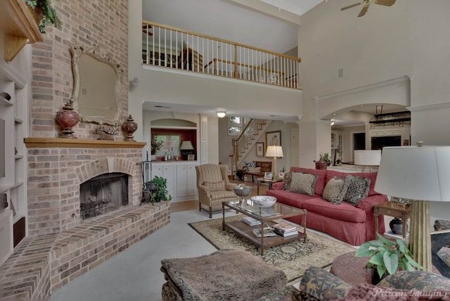 living room featuring a brick fireplace, a high ceiling, and ceiling fan