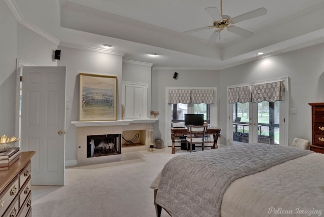 carpeted bedroom with ceiling fan, a raised ceiling, a tiled fireplace, and crown molding