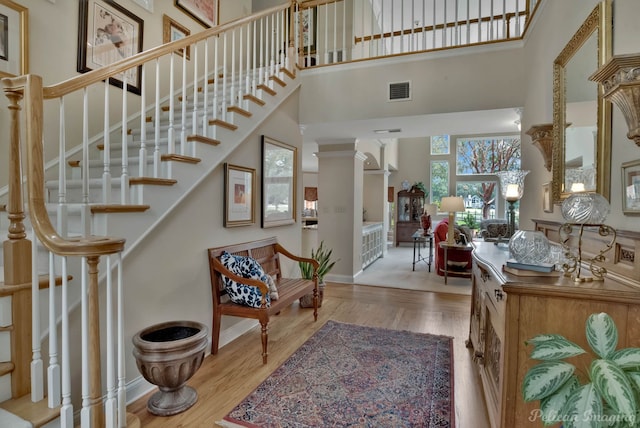 entrance foyer featuring a towering ceiling, light wood-type flooring, and ornate columns