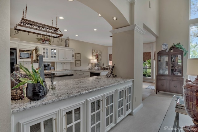 kitchen with light stone counters, white cabinetry, kitchen peninsula, light colored carpet, and a high ceiling