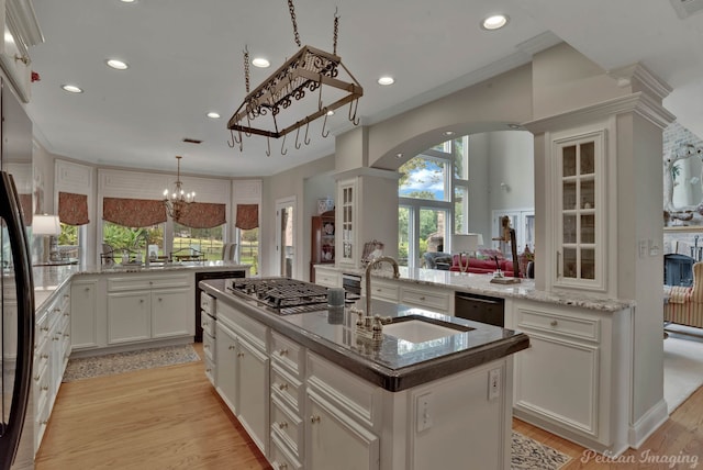 kitchen featuring a notable chandelier, a kitchen island with sink, kitchen peninsula, and light hardwood / wood-style flooring