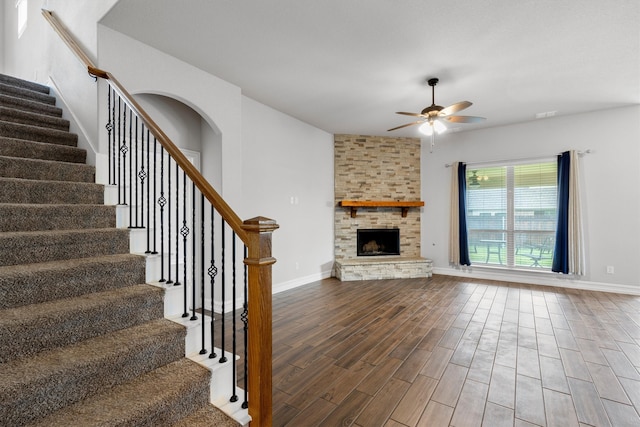 unfurnished living room featuring wood-type flooring, a stone fireplace, and ceiling fan