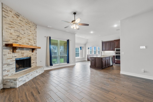 unfurnished living room with a stone fireplace, dark hardwood / wood-style floors, ceiling fan, and sink