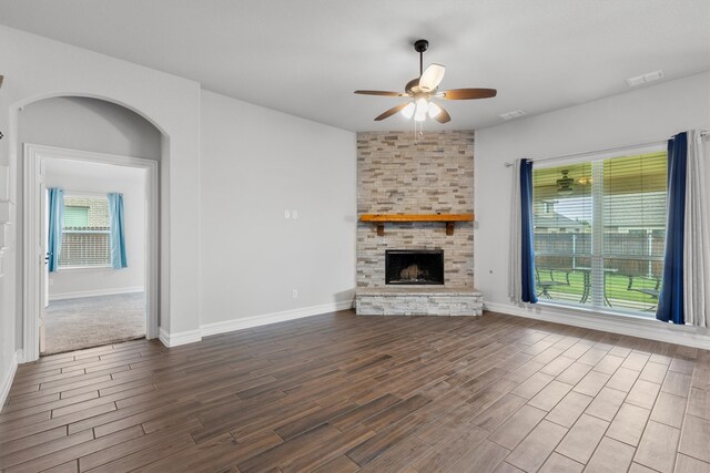 unfurnished living room featuring a healthy amount of sunlight, a stone fireplace, dark hardwood / wood-style floors, and ceiling fan