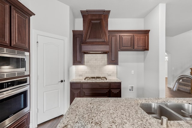 kitchen featuring custom exhaust hood, sink, hardwood / wood-style flooring, stainless steel appliances, and light stone countertops