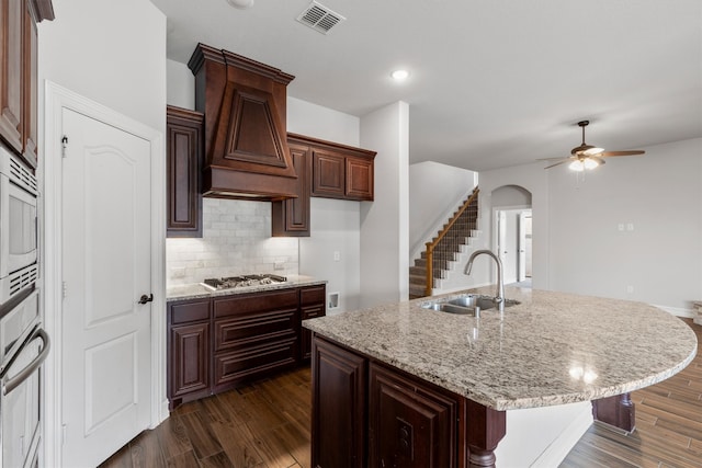 kitchen with appliances with stainless steel finishes, an island with sink, dark hardwood / wood-style flooring, ceiling fan, and sink