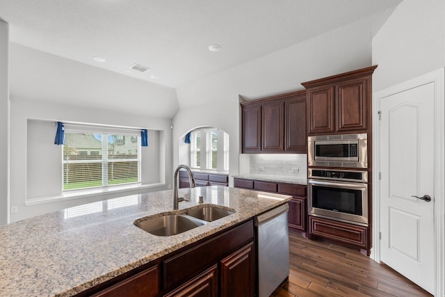 kitchen with appliances with stainless steel finishes, vaulted ceiling, light stone countertops, dark hardwood / wood-style floors, and sink