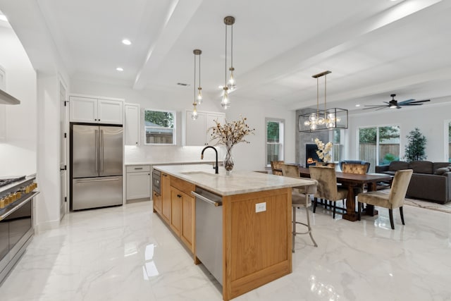 kitchen with appliances with stainless steel finishes, light stone counters, pendant lighting, a kitchen island with sink, and sink