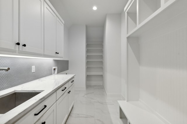 interior space featuring white cabinets, light stone countertops, sink, and tasteful backsplash