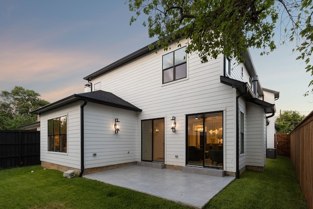 back house at dusk featuring a lawn and a patio area