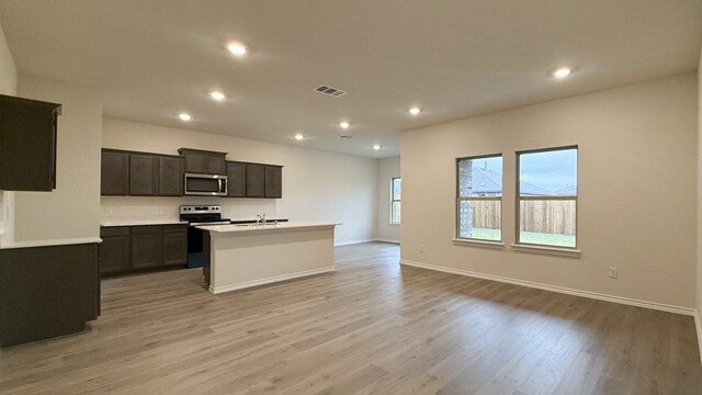 kitchen with dark brown cabinets, stainless steel appliances, light hardwood / wood-style flooring, and an island with sink