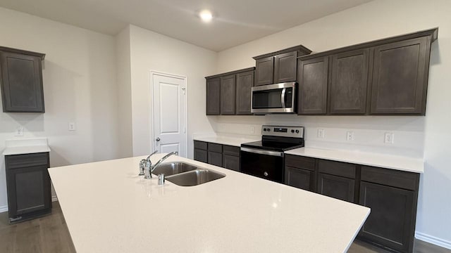 kitchen with appliances with stainless steel finishes, dark hardwood / wood-style flooring, dark brown cabinetry, sink, and an island with sink