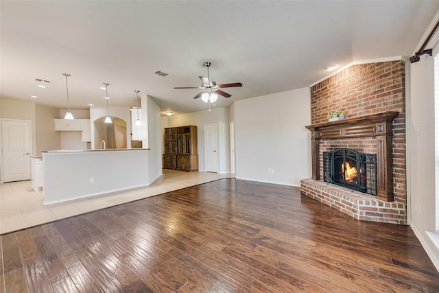 unfurnished living room with hardwood / wood-style flooring, a brick fireplace, and ceiling fan