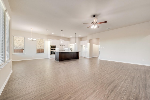 unfurnished living room featuring sink, wood-type flooring, and ceiling fan with notable chandelier