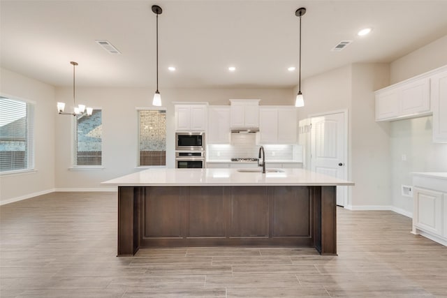 kitchen with built in microwave, sink, a large island with sink, oven, and white cabinets