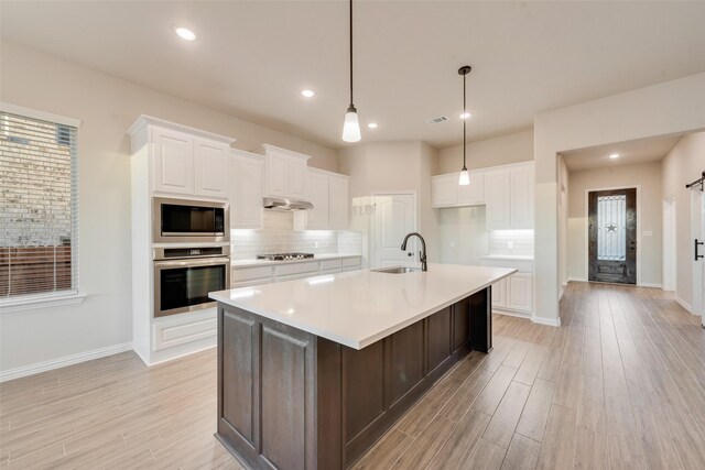 kitchen featuring a center island with sink, sink, a barn door, white cabinetry, and stainless steel appliances