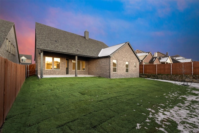 back house at dusk featuring a lawn