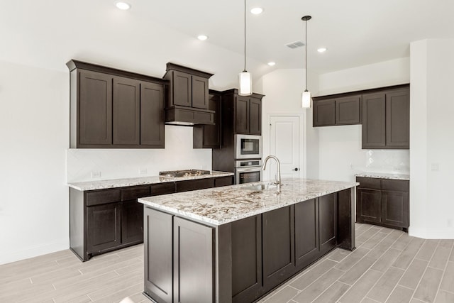 kitchen with pendant lighting, a kitchen island with sink, decorative backsplash, appliances with stainless steel finishes, and light hardwood / wood-style floors