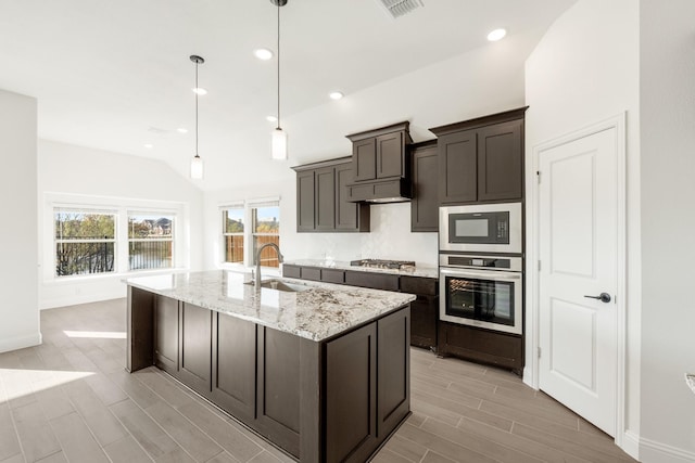 kitchen featuring pendant lighting, sink, light stone countertops, an island with sink, and stainless steel appliances