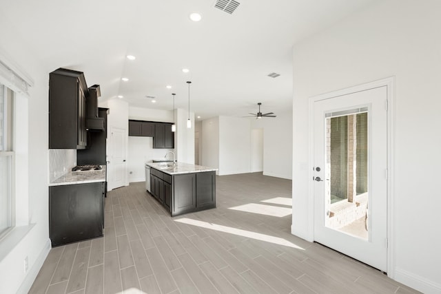 kitchen with ceiling fan, sink, light hardwood / wood-style flooring, hanging light fixtures, and an island with sink