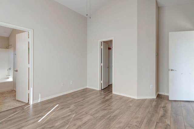 unfurnished bedroom with a walk in closet, light wood-type flooring, high vaulted ceiling, and ensuite bath