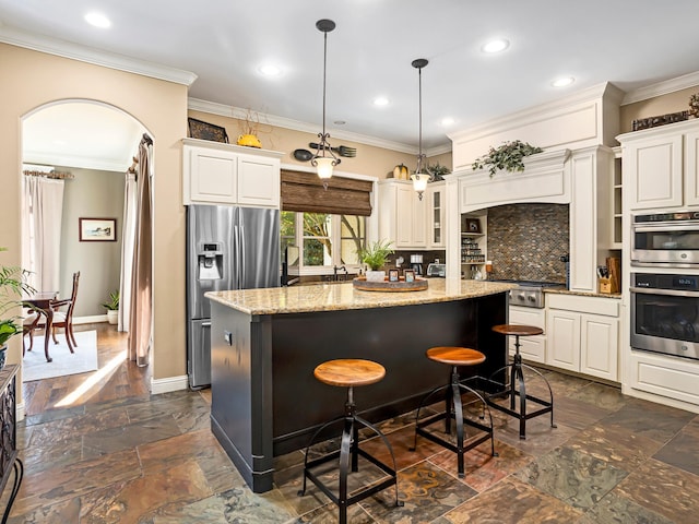 kitchen with light stone counters, ornamental molding, appliances with stainless steel finishes, a center island, and decorative backsplash