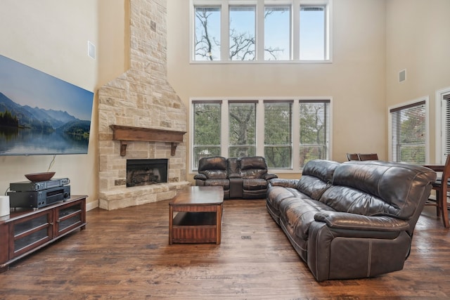 living room featuring a stone fireplace, a towering ceiling, and dark wood-type flooring