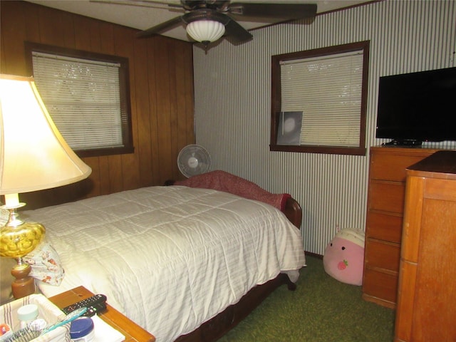 bedroom featuring ceiling fan, wood walls, and dark colored carpet