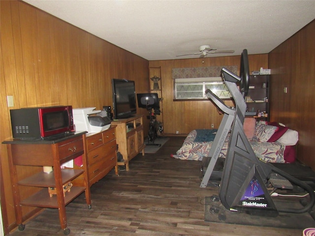 exercise area featuring dark wood-style flooring, wood walls, and a ceiling fan