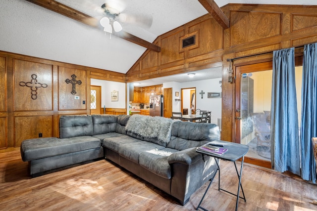 living room featuring hardwood / wood-style floors, ceiling fan, wood walls, and beam ceiling