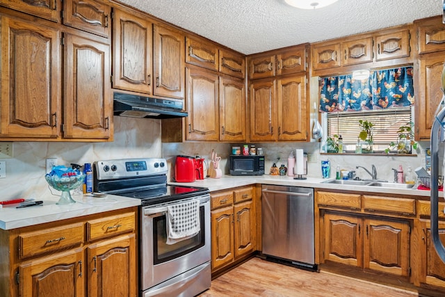 kitchen with sink, light hardwood / wood-style floors, a textured ceiling, decorative backsplash, and appliances with stainless steel finishes