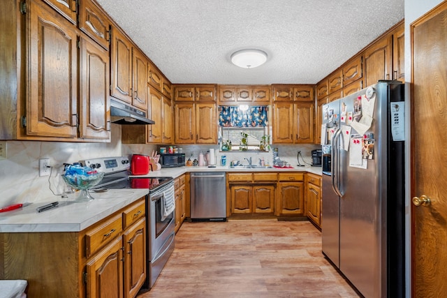 kitchen with sink, stainless steel appliances, a textured ceiling, and light wood-type flooring