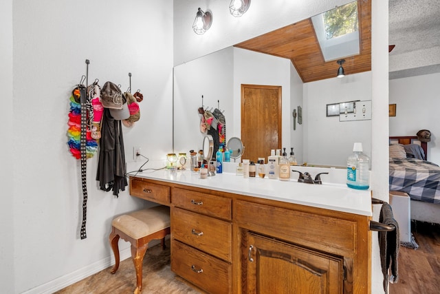 bathroom with vaulted ceiling with skylight, vanity, wood-type flooring, and a textured ceiling