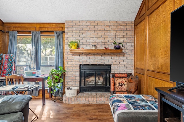 living room featuring a brick fireplace, a textured ceiling, vaulted ceiling, wooden walls, and hardwood / wood-style floors