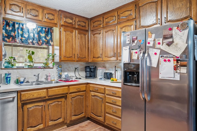 kitchen featuring sink, light hardwood / wood-style flooring, a textured ceiling, appliances with stainless steel finishes, and tasteful backsplash