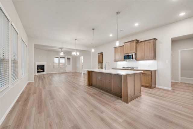 kitchen with a kitchen island with sink, sink, decorative light fixtures, and light hardwood / wood-style flooring