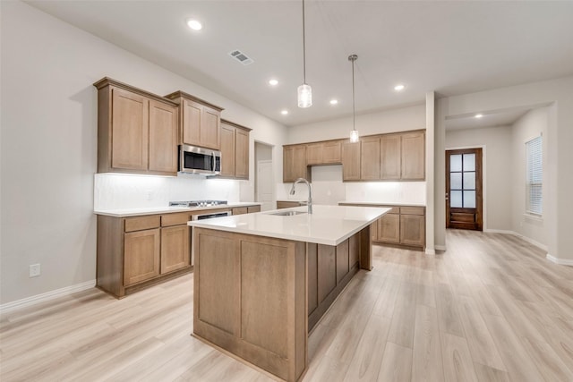 kitchen with pendant lighting, sink, a kitchen island with sink, light hardwood / wood-style floors, and stainless steel appliances