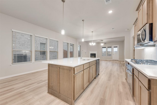 kitchen featuring decorative light fixtures, sink, a kitchen island with sink, stainless steel appliances, and light wood-type flooring